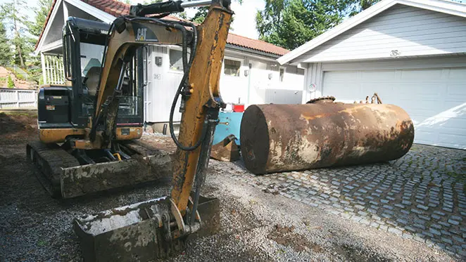 Gravemaskin som graver opp en gammel oljetank som skal byttes ut med varmepumpe fra NIBE