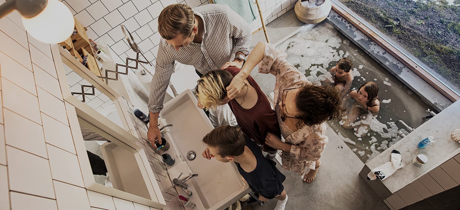 En familie der noen pusser tennene på badet, mens andre bader i bakgrunnen